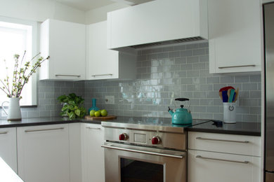 Example of a large 1950s l-shaped medium tone wood floor and exposed beam enclosed kitchen design in Boston with an undermount sink, recessed-panel cabinets, white cabinets, quartz countertops, gray backsplash, glass tile backsplash, stainless steel appliances, an island and gray countertops