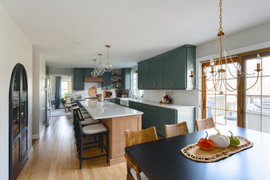 Large trendy u-shaped light wood floor and orange floor eat-in kitchen photo in Other with a farmhouse sink, shaker cabinets, green cabinets, quartz countertops, white backsplash, subway tile backsplash, stainless steel appliances, an island and white countertops