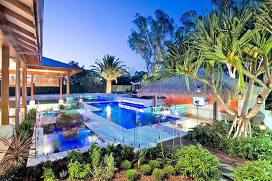 Expansive beach style backyard custom-shaped lap pool in Brisbane with a pool house and natural stone pavers.