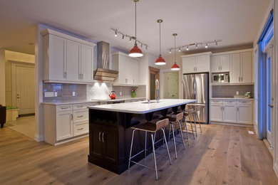 Large trendy l-shaped light wood floor and beige floor eat-in kitchen photo in Edmonton with an undermount sink, shaker cabinets, white cabinets, quartz countertops, gray backsplash, subway tile backsplash, stainless steel appliances and an island