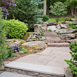 This is an example of a traditional sloped garden in New York with natural stone pavers and with rock feature.