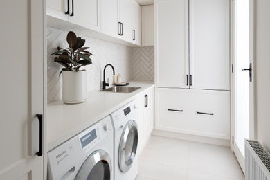 Photo of a large transitional single-wall laundry room in Melbourne with a drop-in sink, raised-panel cabinets, white cabinets, quartz benchtops, white splashback, matchstick tile splashback, medium hardwood floors, brown floor and white benchtop.
