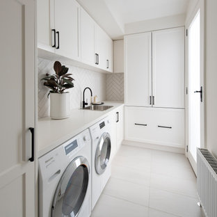 Photo of a large transitional single-wall laundry room in Melbourne with a drop-in sink, raised-panel cabinets, white cabinets, quartz benchtops, white splashback, matchstick tile splashback, medium hardwood floors, brown floor and white benchtop.