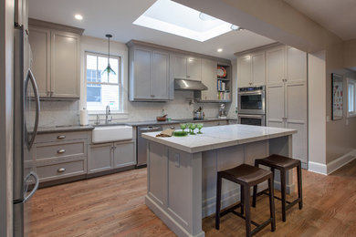 Example of a transitional single-wall medium tone wood floor eat-in kitchen design in DC Metro with a farmhouse sink, shaker cabinets, gray cabinets, marble countertops, white backsplash, ceramic backsplash, stainless steel appliances and an island