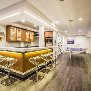 ニューヨークの大きいモダンスタイルのおしゃれな着席型バー (アンダーカウンターシンク、ガラス扉のキャビネット、中間色木目調キャビネット、人工大理石カウンター、白いキッチンパネル、塗装フローリング、茶色い床) の写真