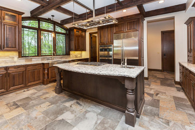 Large 1960s u-shaped slate floor enclosed kitchen photo in Other with a farmhouse sink, raised-panel cabinets, dark wood cabinets, quartz countertops, beige backsplash, stone tile backsplash, stainless steel appliances and an island
