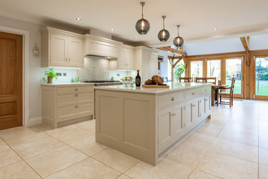 This is an example of a large country l-shaped eat-in kitchen in Hertfordshire with an integrated sink, beaded inset cabinets, grey cabinets, quartzite benchtops, grey splashback, glass sheet splashback, stainless steel appliances, ceramic floors, with island, beige floor and white benchtop.