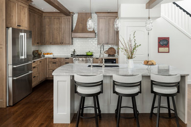Example of a mid-sized french country l-shaped dark wood floor, brown floor and exposed beam kitchen pantry design in Portland with a farmhouse sink, recessed-panel cabinets, medium tone wood cabinets, quartzite countertops, white backsplash, subway tile backsplash, stainless steel appliances, an island and multicolored countertops