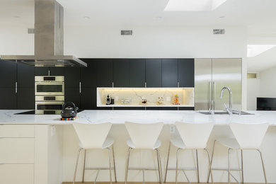 Photo of a large contemporary single-wall open plan kitchen in Los Angeles with an undermount sink, flat-panel cabinets, white cabinets, quartz benchtops, white splashback, stone slab splashback, stainless steel appliances, light hardwood floors, with island, brown floor and white benchtop.