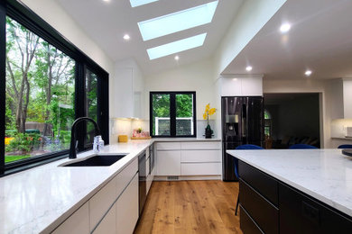Inspiration for a huge modern medium tone wood floor and vaulted ceiling open concept kitchen remodel in Boston with an undermount sink, flat-panel cabinets, white cabinets, quartz countertops, white backsplash, glass sheet backsplash, black appliances, an island and white countertops