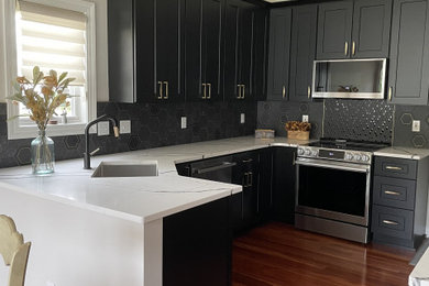 Mid-sized trendy u-shaped medium tone wood floor, brown floor and vaulted ceiling eat-in kitchen photo in Grand Rapids with shaker cabinets, black cabinets, quartz countertops, mosaic tile backsplash, stainless steel appliances, no island and multicolored countertops