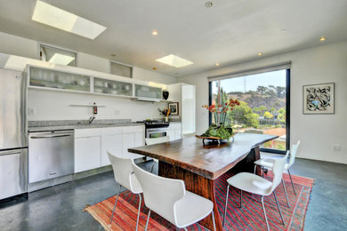 Mid-sized trendy single-wall concrete floor and gray floor eat-in kitchen photo in Los Angeles with a drop-in sink, flat-panel cabinets, white cabinets, granite countertops, stainless steel appliances, gray backsplash, stone slab backsplash and no island