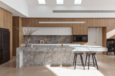 Photo of a mid-sized contemporary l-shaped kitchen in Sydney with an undermount sink, flat-panel cabinets, white cabinets, grey splashback, stone slab splashback, black appliances, with island, beige floor and grey benchtop.