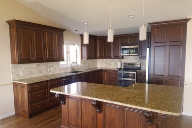 This is an example of a mid-sized traditional l-shaped eat-in kitchen in Little Rock with an undermount sink, raised-panel cabinets, medium wood cabinets, granite benchtops, beige splashback, stone tile splashback, stainless steel appliances, light hardwood floors, with island, brown floor and beige benchtop.