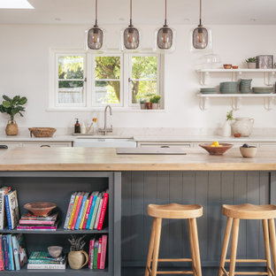 Medium sized rural open plan kitchen in Gloucestershire with a belfast sink, recessed-panel cabinets, beige cabinets, quartz worktops, slate flooring, grey floors, beige worktops and an island.