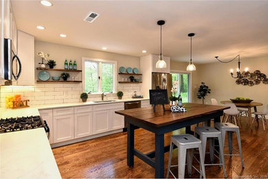 Example of a mid-sized transitional l-shaped medium tone wood floor and brown floor enclosed kitchen design in New York with a single-bowl sink, shaker cabinets, white cabinets, quartzite countertops, white backsplash, subway tile backsplash, stainless steel appliances, an island and gray countertops