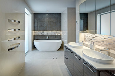 Inspiration for a large contemporary bathroom in Adelaide with a drop-in sink, flat-panel cabinets, dark wood cabinets, solid surface benchtops, a freestanding tub, beige tile, porcelain tile, beige walls and porcelain floors.