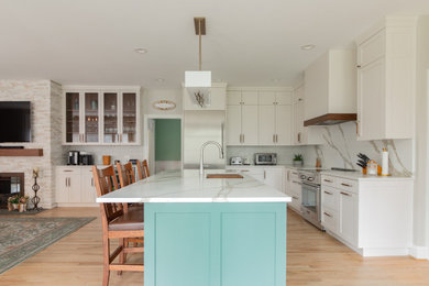 Example of a large transitional l-shaped light wood floor and brown floor open concept kitchen design in Other with an undermount sink, shaker cabinets, quartz countertops, white backsplash, quartz backsplash, stainless steel appliances, an island, white countertops and white cabinets