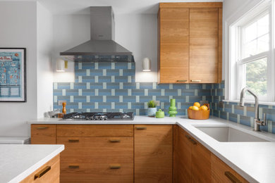 ボストンにあるミッドセンチュリースタイルのおしゃれなアイランドキッチン (アンダーカウンターシンク、フラットパネル扉のキャビネット、中間色木目調キャビネット、クオーツストーンカウンター、青いキッチンパネル、セラミックタイルのキッチンパネル、シルバーの調理設備、磁器タイルの床、グレーの床、白いキッチンカウンター) の写真