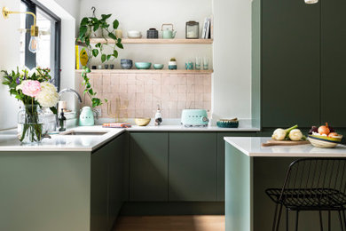 Large contemporary l-shaped open plan kitchen in London with a single-bowl sink, green cabinets, white splashback, coloured appliances, light hardwood flooring, an island, brown floors and white worktops.