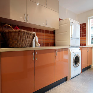 Photo of a large modern galley separated utility room in Melbourne with a submerged sink, flat-panel cabinets, engineered stone countertops, white walls, porcelain flooring, a stacked washer and dryer and orange cabinets.