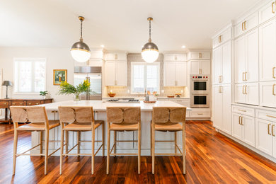 Open concept kitchen - large transitional l-shaped dark wood floor and brown floor open concept kitchen idea in Denver with a farmhouse sink, shaker cabinets, beige cabinets, quartz countertops, beige backsplash, ceramic backsplash, stainless steel appliances, an island and white countertops