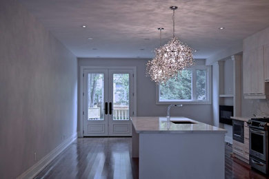 Example of a large trendy single-wall medium tone wood floor kitchen design in Toronto with an undermount sink, shaker cabinets, white cabinets, quartz countertops, multicolored backsplash, stone slab backsplash, stainless steel appliances and an island