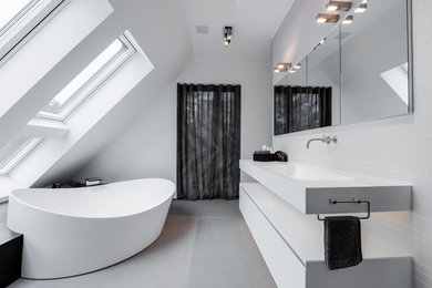 Photo of a large contemporary bathroom in Dusseldorf with flat-panel cabinets, white cabinets, a freestanding tub, a curbless shower, a wall-mount toilet, white tile, ceramic tile, white walls, pebble tile floors, a drop-in sink, solid surface benchtops, grey floor and white benchtops.