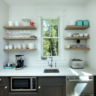 Идея дизайна: маленькая линейная кухня в стиле кантри с кладовкой, фасадами с утопленной филенкой, темными деревянными фасадами, врезной раковиной, белым фартуком, фартуком из плитки кабанчик, техникой под мебельный фасад, светлым паркетным полом, коричневым полом, столешницей из кварцевого композита и белой столешницей без острова