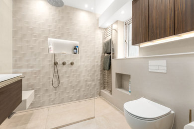 Inspiration for a medium sized contemporary ensuite bathroom in Berkshire with flat-panel cabinets, brown cabinets, a walk-in shower, a wall mounted toilet, beige tiles, ceramic tiles, beige walls, porcelain flooring, a built-in sink, solid surface worktops, beige floors, an open shower, white worktops, a feature wall, a single sink and a floating vanity unit.