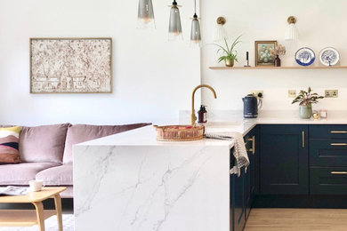 Medium sized contemporary l-shaped open plan kitchen in Other with a single-bowl sink, shaker cabinets, blue cabinets, quartz worktops, white splashback, stone slab splashback, black appliances, an island, white worktops and feature lighting.