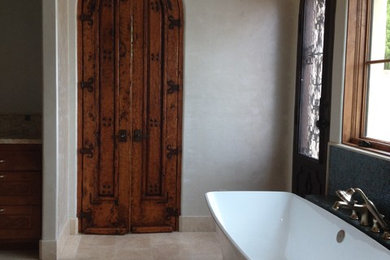 Example of a huge eclectic master beige tile travertine floor freestanding bathtub design in Dallas with raised-panel cabinets, brown cabinets, white walls and onyx countertops