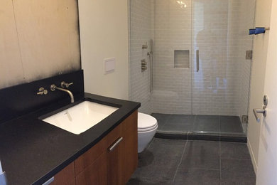 Diseño de cuarto de baño minimalista con ducha abierta, baldosas y/o azulejos grises, aseo y ducha, encimera de granito, ducha con puerta con bisagras y encimeras negras