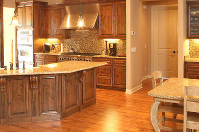 Inspiration for a large craftsman l-shaped medium tone wood floor and brown floor eat-in kitchen remodel in Phoenix with a farmhouse sink, raised-panel cabinets, dark wood cabinets, granite countertops, multicolored backsplash, mosaic tile backsplash, stainless steel appliances, an island and multicolored countertops