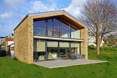 Ejemplo de fachada de casa minimalista de tamaño medio de dos plantas con revestimiento de piedra, tejado a dos aguas y tejado de teja de barro