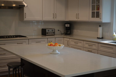 Inspiration for a mid-sized transitional l-shaped eat-in kitchen remodel in Chicago with recessed-panel cabinets, quartz countertops, white backsplash, ceramic backsplash, stainless steel appliances, an island and gray countertops