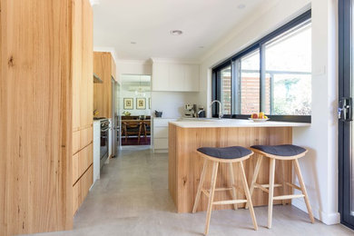 This is an example of a mid-sized contemporary galley separate kitchen in Canberra - Queanbeyan with a double-bowl sink, flat-panel cabinets, light wood cabinets, laminate benchtops, white splashback, porcelain splashback, stainless steel appliances, ceramic floors, a peninsula and grey floor.