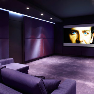 Cette image montre une grande salle de cinéma design fermée avec un mur violet, moquette et un écran de projection.