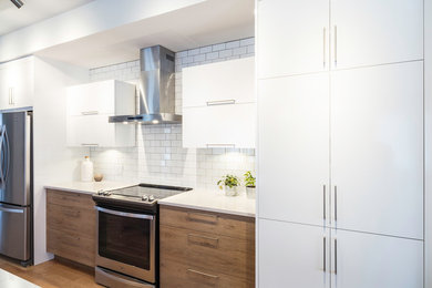 Inspiration for a mid-sized contemporary galley kitchen in Montreal with flat-panel cabinets, white cabinets, quartz benchtops, white splashback, subway tile splashback, stainless steel appliances and light hardwood floors.