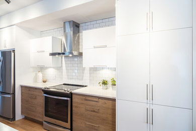 Kitchen - mid-sized contemporary galley light wood floor kitchen idea in Montreal with flat-panel cabinets, white cabinets, quartz countertops, white backsplash, subway tile backsplash and stainless steel appliances