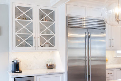 Large transitional l-shaped dark wood floor and brown floor kitchen photo in New York with a farmhouse sink, shaker cabinets, white cabinets, marble countertops, white backsplash, marble backsplash, stainless steel appliances and an island