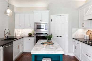 This is an example of a medium sized traditional l-shaped kitchen/diner in Austin with a submerged sink, white cabinets, granite worktops, white splashback, stainless steel appliances, light hardwood flooring, an island, brown floors and multicoloured worktops.