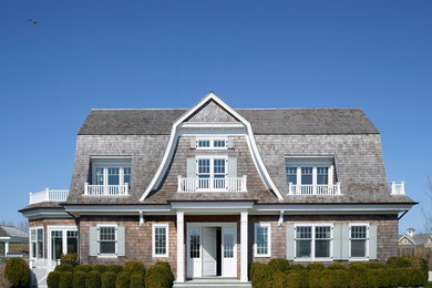 This is an example of a large and brown coastal two floor house exterior in New York with wood cladding and a mansard roof.