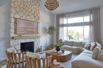 Example of a beach style medium tone wood floor, brown floor and vaulted ceiling living room design in Los Angeles with a standard fireplace, a stone fireplace and white walls
