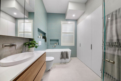 Inspiration for a large contemporary kids bathroom in Sydney with furniture-like cabinets, light wood cabinets, a freestanding tub, a corner shower, a one-piece toilet, blue tile, subway tile, grey walls, ceramic floors, a drop-in sink, solid surface benchtops, beige floor, a hinged shower door, white benchtops, a niche, a single vanity and a floating vanity.