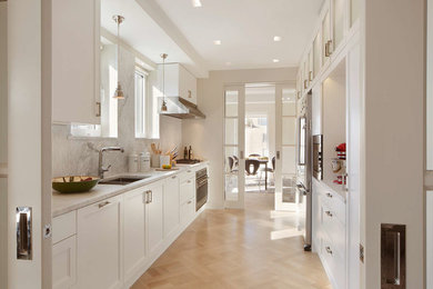 Open concept kitchen - large contemporary galley medium tone wood floor open concept kitchen idea in New York with an undermount sink, glass-front cabinets, white cabinets, granite countertops, gray backsplash, stone slab backsplash and stainless steel appliances
