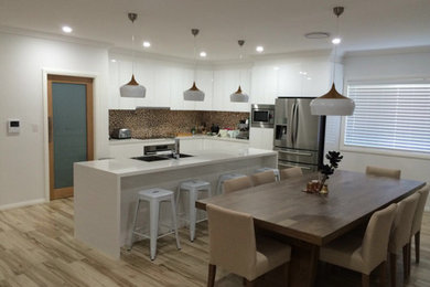 Design ideas for a large contemporary galley kitchen/diner in Sydney with a submerged sink, white cabinets, composite countertops, brown splashback, glass tiled splashback, stainless steel appliances, ceramic flooring, an island, brown floors and white worktops.
