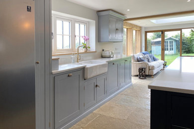 Large contemporary galley kitchen/diner in Other with a belfast sink, shaker cabinets, blue cabinets, marble worktops, white splashback, marble splashback, stainless steel appliances, limestone flooring, an island, beige floors and white worktops.