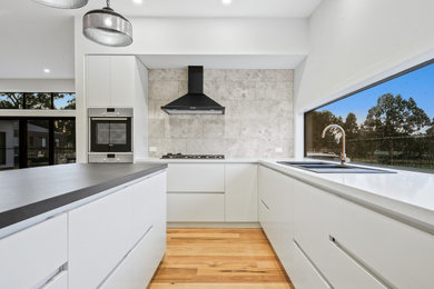 Inspiration for a mid-sized contemporary l-shaped eat-in kitchen in Other with an undermount sink, shaker cabinets, white cabinets, quartz benchtops, grey splashback, limestone splashback, black appliances, light hardwood floors, with island, brown floor, black benchtop and vaulted.