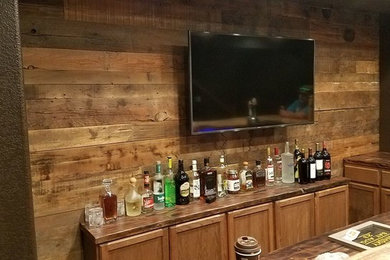 Design ideas for a large country l-shaped seated home bar in Denver with recessed-panel cabinets, dark wood cabinets, wood benchtops, an undermount sink, brown splashback, timber splashback, laminate floors and brown floor.